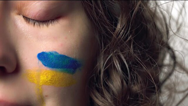 Tears of pain with Ukrainian flag on cheek. Crying hopeful sad powerless scared emotional woman with Ukraine flag on her face. Russian-Ukrainian war. Save Ukraine and stop the war. Pray for Ukraine
