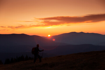 Tourist in mountains at sunset. Orange sky. Silhouette of mountains peaks
