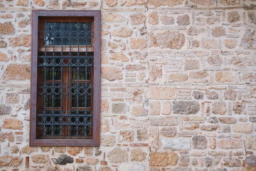 Stone wall with a window with brown wooden frames on an ancient building