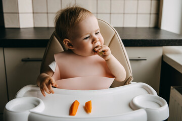10 months old baby sitting in high chair, with a silicone bib, eating avocado.