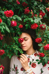 Beautiful brunette female close eyes, inhale the fragrance among red rose flowers.