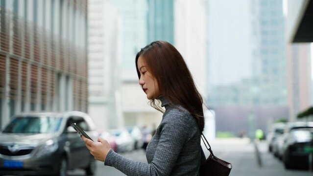 Charming young asian business woman walking in the city street looking at mobile phone side view slow motion clip