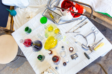 Various chemicals, medical instruments and a hacksaw with bloody bandages on a table in a secret biolab