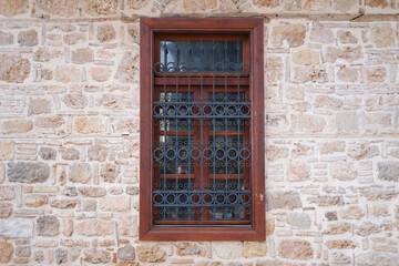 Vintage window with wooden frames and black grate on a stone antique wall of the building