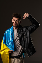 Obraz na płótnie Canvas Young man holding a flag of Ukraine smiling confident with crossed arms ion a black background.