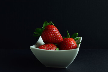 Strawberries in a bowl, black background and copy space.