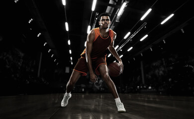 African-american young basketball player in action and motion in flashlights over dark gym...