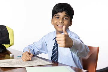 young boy from primary school studying seating writing thumbs up in the classroom isolated on white background