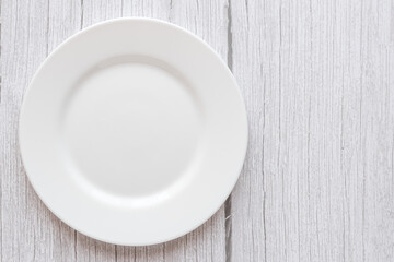 Plate on the background of a wooden tabletop. View from above. Small flat round white plate. Place for text.