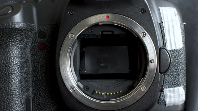 A close up shot of the hand of a Photographer as he removes the protective cap of a DSLR camera body to reveal the inner workings of the mechanical shutter and