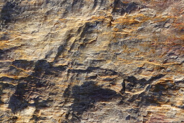 Rough bust fractured gray orange detail stone wall structure surface.