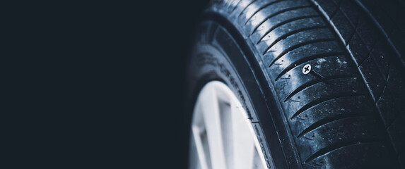 A close-up shows a sharp metal screw piercing an automobile tire,black background and copy space