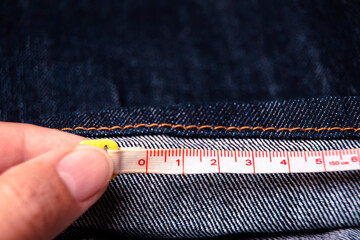 Hand of tailor measure the length of the jeans with a measuring tape - obrazy, fototapety, plakaty