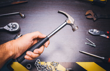 Metal hammer tool on the hand of mechanic with mechanic tools on backdrop