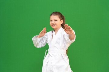 a little girl in a white kimono does a warm-up before training on a green background. child is studying martial arts