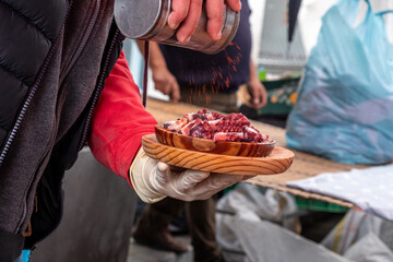 Hand of a man pouring paprika on a portion of Pulpo a feira, a popular recipe for octopus in...