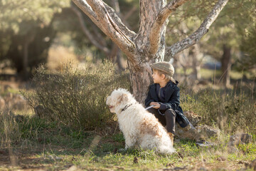 a little boy in vintage clothes walks in nature with a white shaggy dog in spring..