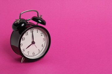 vintage old black alarm clock on pink background	