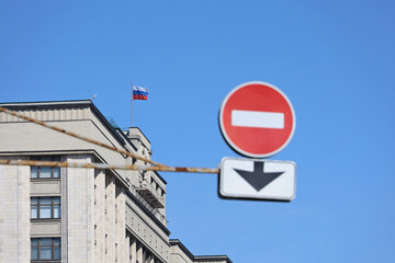 State Duma of Russia with Russian flag and stop sign on the foreground against blue sky. Concept of economic sanctions due to the russian special military operation in Ukraine
