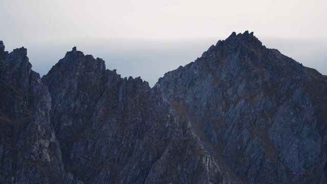 An outlandish landscape of the Andoya rocky coast near Bleik. Dark jagged rocks against the pale sky. Slow-motion, orbit shot.