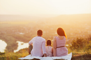 Young family sitting and watching the sunset over the countryside. They relax during their vacation and enjoy the sunset together.