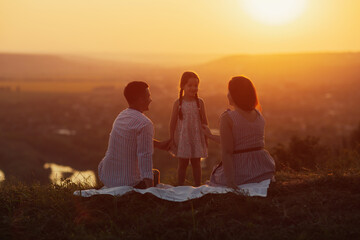 Happy family at amazing sunset. Father, mother and cute daughter relaxing in nature.