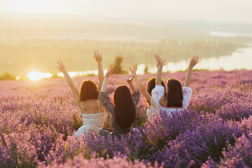Beautiful girlfriends having picnic in the lavender field in summer sunset. They sitting with hands...