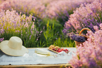 Wicker basket with bouquet of lavender, tasty berries and wine for romantic picnic in lavender...