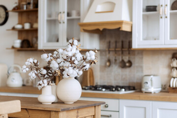 stylish kitchen in the old style, light, wooden, with stone tiles. Cotton in a vase. Composition in a ceramic pot.