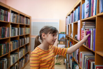 Waist up portrait of schoolgirl choosing books in school library, copy space