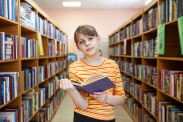Child  near bookshelves and reading   at school's library.