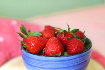 Bowl of fresh strawberries on a bed with colorful bedding. Selective focus.