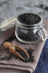 Fototapeta na wymiar Indian spice Black cumin (nigella sativa or kalonji) seeds in glass jar with a wooden scoop close up