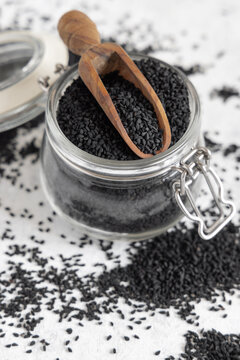 Indian spice Black cumin (nigella sativa or kalonji) seeds in glass jar with a wooden scoop close up