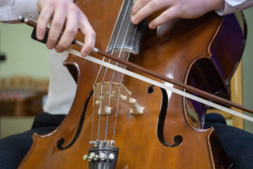 a person plays the cello, both hands and a bow are visible