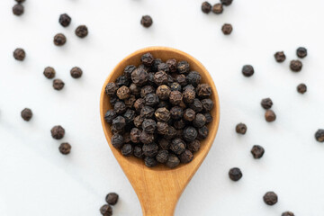 Black peppercorn with a wooden spoon on white background. Composition isolated over the white background.