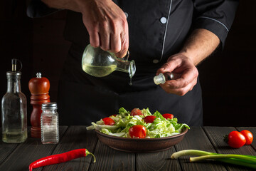 Professional chef pours olive oil into a bowl of salad. Cooking tasty and healthy food with set of vitamins