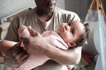 Medium close-up of loving African American father holding his baby daughter in arms lulling her