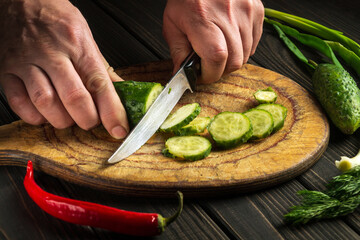 The chef cuts cucumber on a cutting board. Close-up of a cook hands while preparing a salad with fresh vegetables