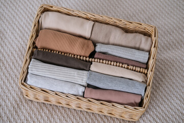 Wicker container with clothes on the bed. Vertical clothing storage. Concept of minimalism lifestyle
