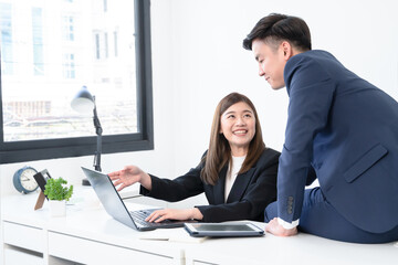 Fototapeta premium Asian young businesswoman wear formal suit working with colleagues man presenting new ideas on laptop with smiling face. Happy business people in workplace where they was accepted concept