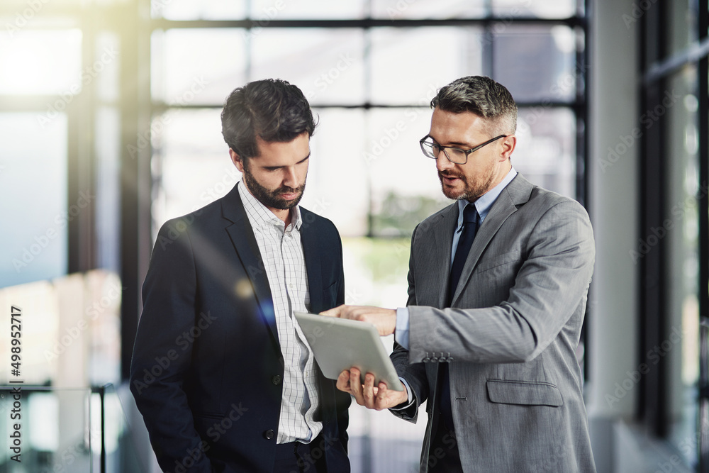 Poster Running an idea past a trusted colleague. Shot of two businessmen looking over a tablet in the office.