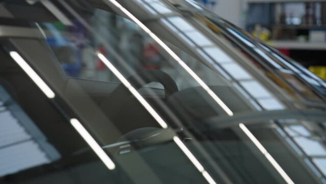 Lights reflecting on front windshield of a parking car in workshop.