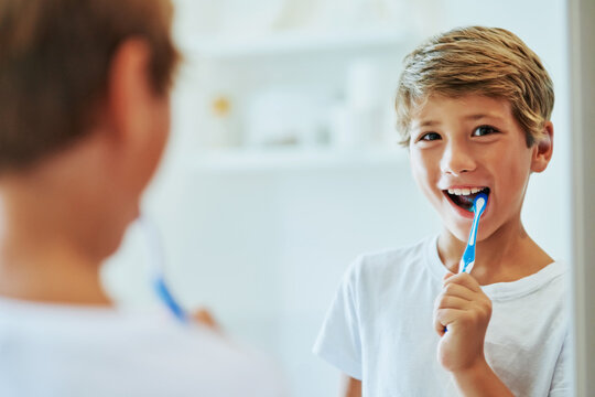 Keeping My Teeth Strong. Shot Of A Cheerful Young Boy Looking At His Reflection In A Mirror While Brushing His Teeth In The Bathroom At Home During The Day.