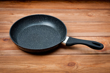 A round frying pan with a plastic handle is a utensil for frying food. Taken against the backdrop of a wooden table surface.