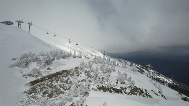 Amazing aerial view from drone ski lift moving through clouds in winter resort. Ski elevator on ropeway transporting people in ski resort. Drone view fogy white mountain on blue sky landscape