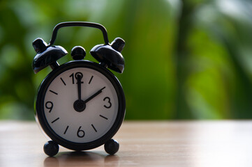 Black alarm clock isolated on blurred nature background. The clock set at 2 o'clock. Copy space concept