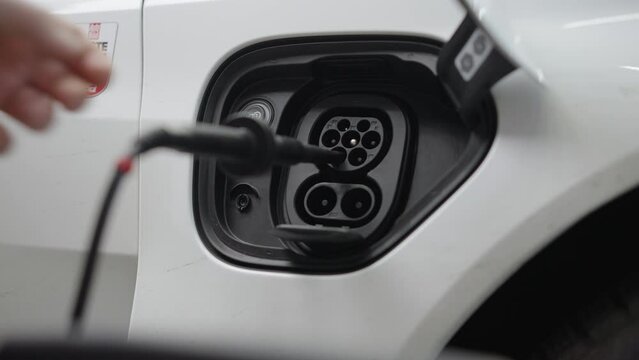 Hand putting measuring device into charging port of white electric car
