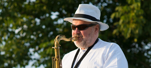 Man playing jazz music on saxophone in the spring nature on a sunny day