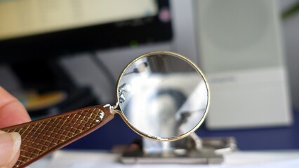 A round antique magnifying glass held between the thumb and forefinger